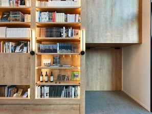 A library with wooden shelves filled with books and a few bottles. - ibis Styles La Roche-sur-Yon (Mouilleron-le-Captif)
