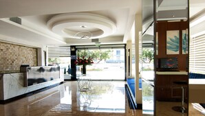 A modern hotel lobby with a marble reception desk, a large vase of flowers, and a seating area with a blue sofa. - LYZ Business Hotel (Lima)