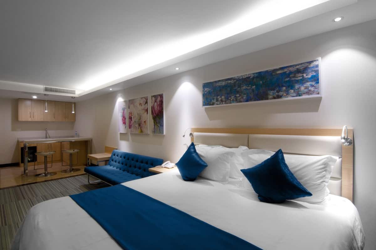A modern hotel room with a large bed, a small kitchenette, and a seating area.