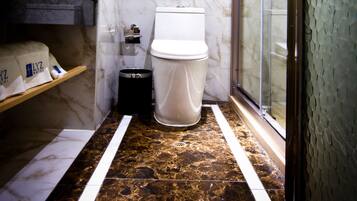 A bathroom with a marble floor, a toilet, a shower enclosure, and a sink with a towel dispenser.