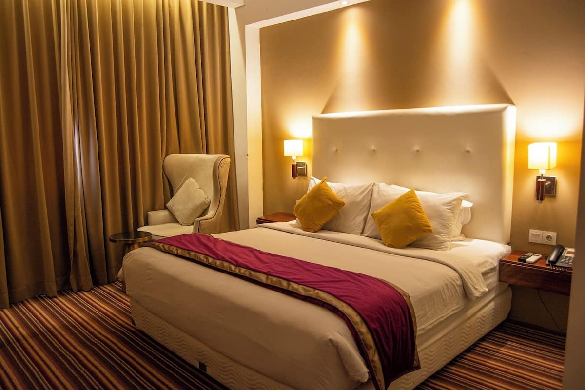 A hotel room with a large bed, a chair, two bedside lamps, and a striped carpet.