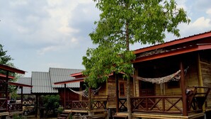 A rustic wooden cabin with a porch, a hammock, and a tree in front. - Family Huts (Pai)