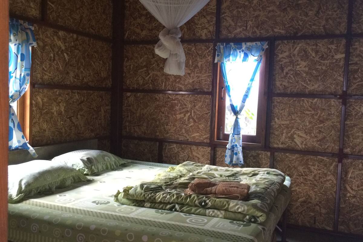 Ein Zimmer mit Bett, Holzwänden und einem Fenster mit Vorhängen.