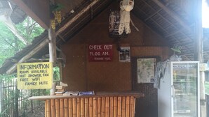 A rustic hut with a bamboo counter, a signboard with information, a refrigerator, and a hanging light fixture. - Family Huts (Pai)