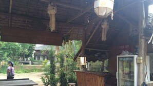 A rustic outdoor seating area with a wooden bench, a stool, and a refrigerator labeled "COLD DRINKS" with various beverages. - Family Huts (Pai)