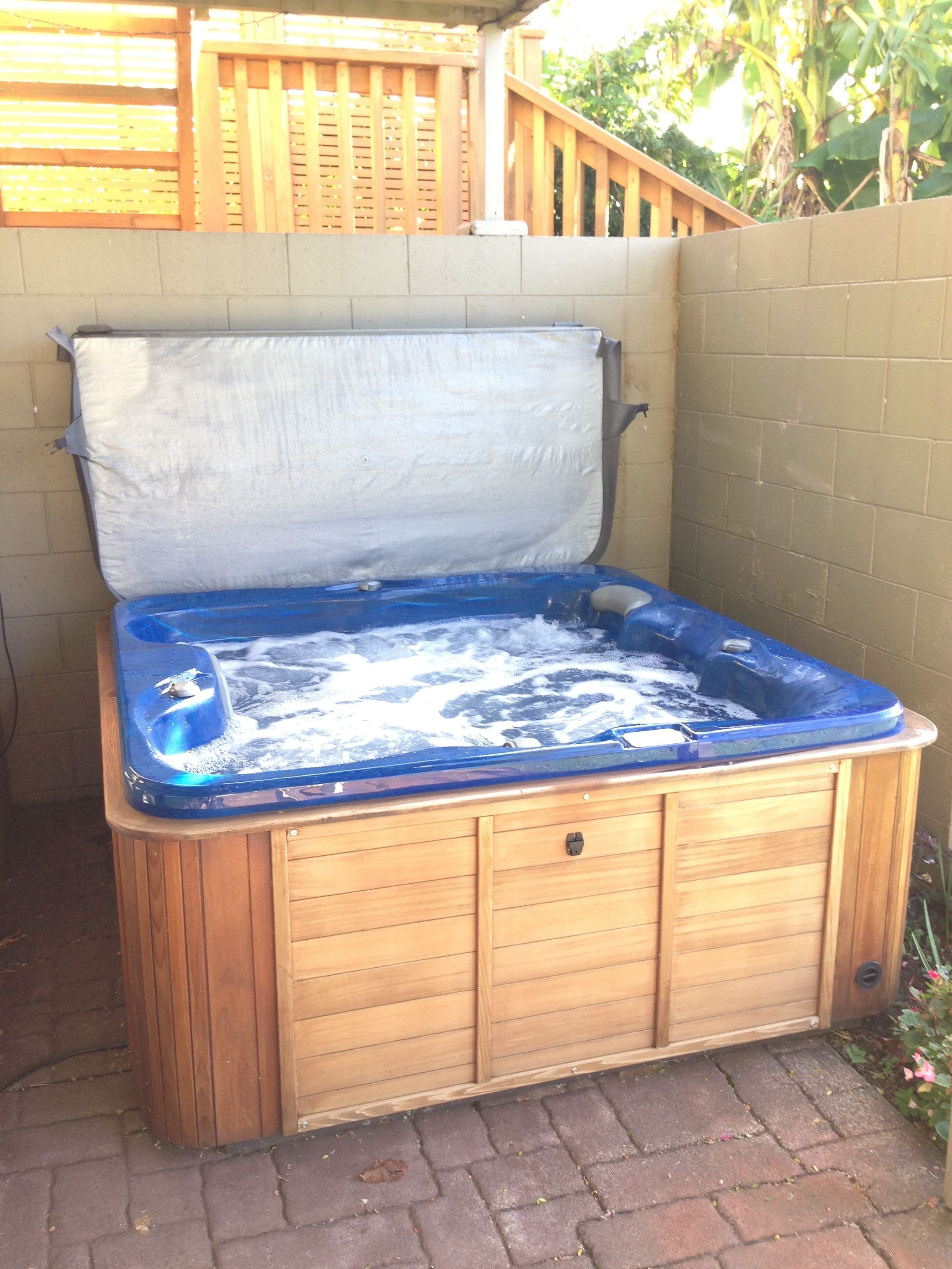 Un bain à remous en bois, avec un intérieur bleu, un couvercle blanc et une base en bois.