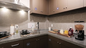 Uma cozinha moderna com bancada de granito, eletrodomésticos de aço inoxidável e painel de azulejos hexagonais.
