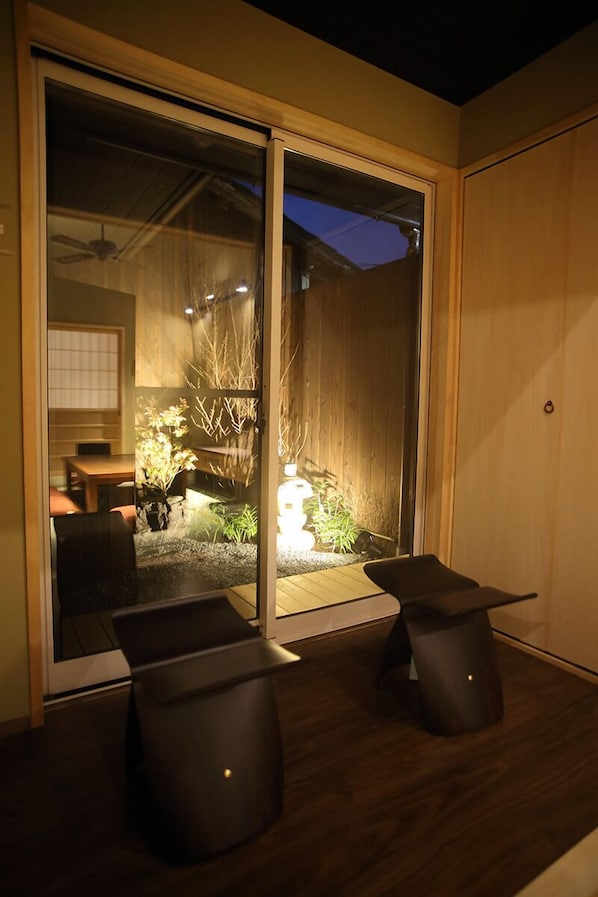 A modern room with a sliding glass door leading to a garden. There are two black chairs and a small table.