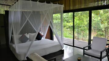 Una habitación con cama bajo un dosel, un balcón con vistas a zonas verdes y un rincón de estar con una mesa.