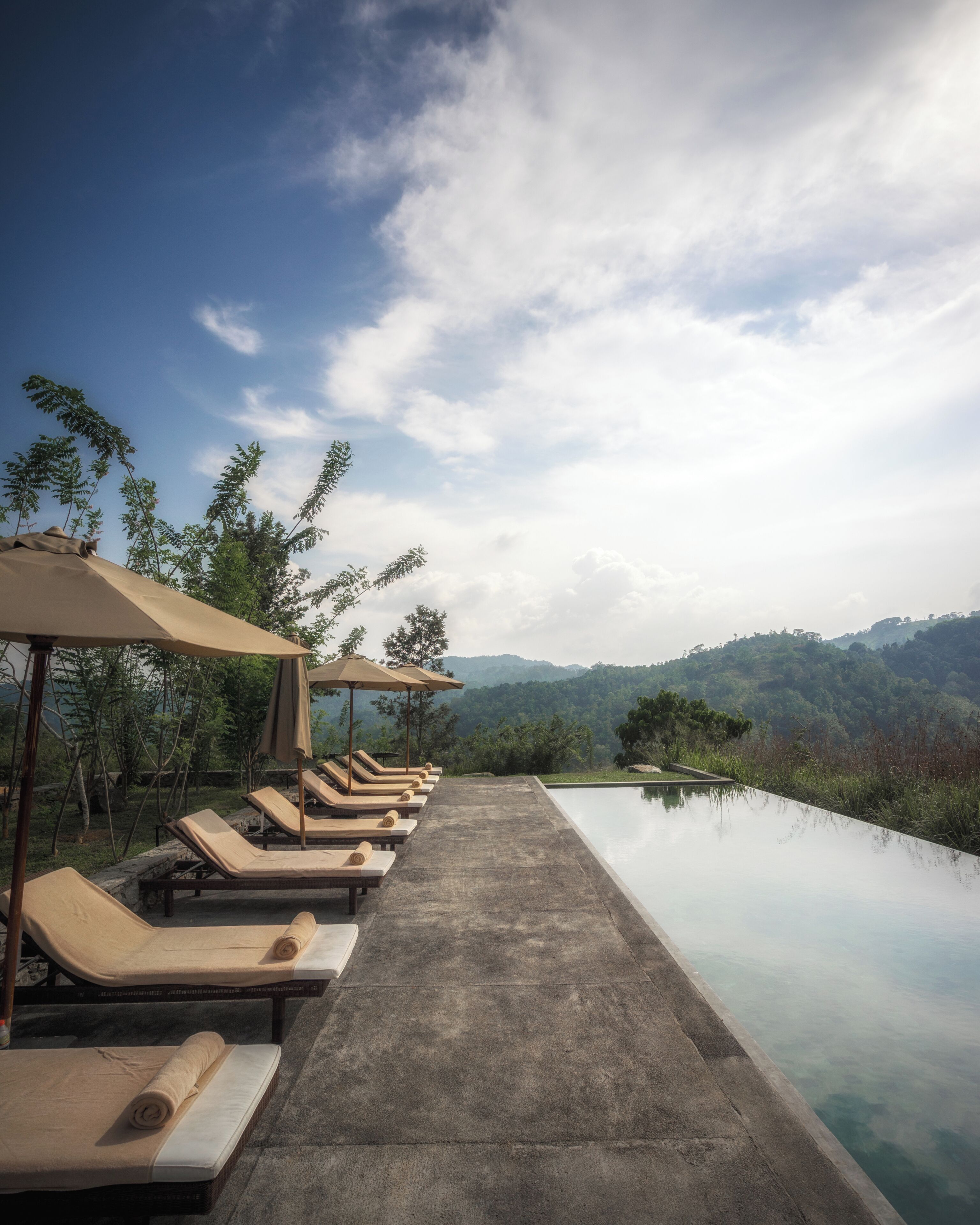 A poolside area with lounge chairs and umbrellas, overlooking a mountainous landscape.