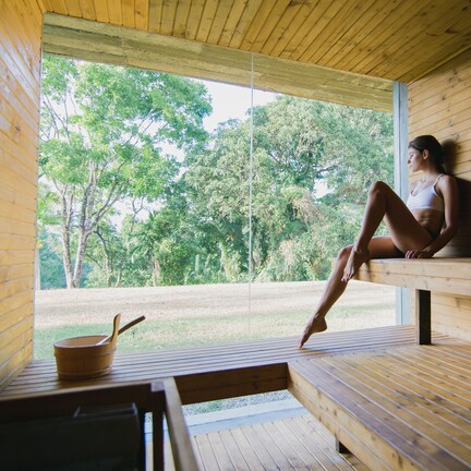 A wooden sauna with a bench, a wooden table, and a view of trees outside.