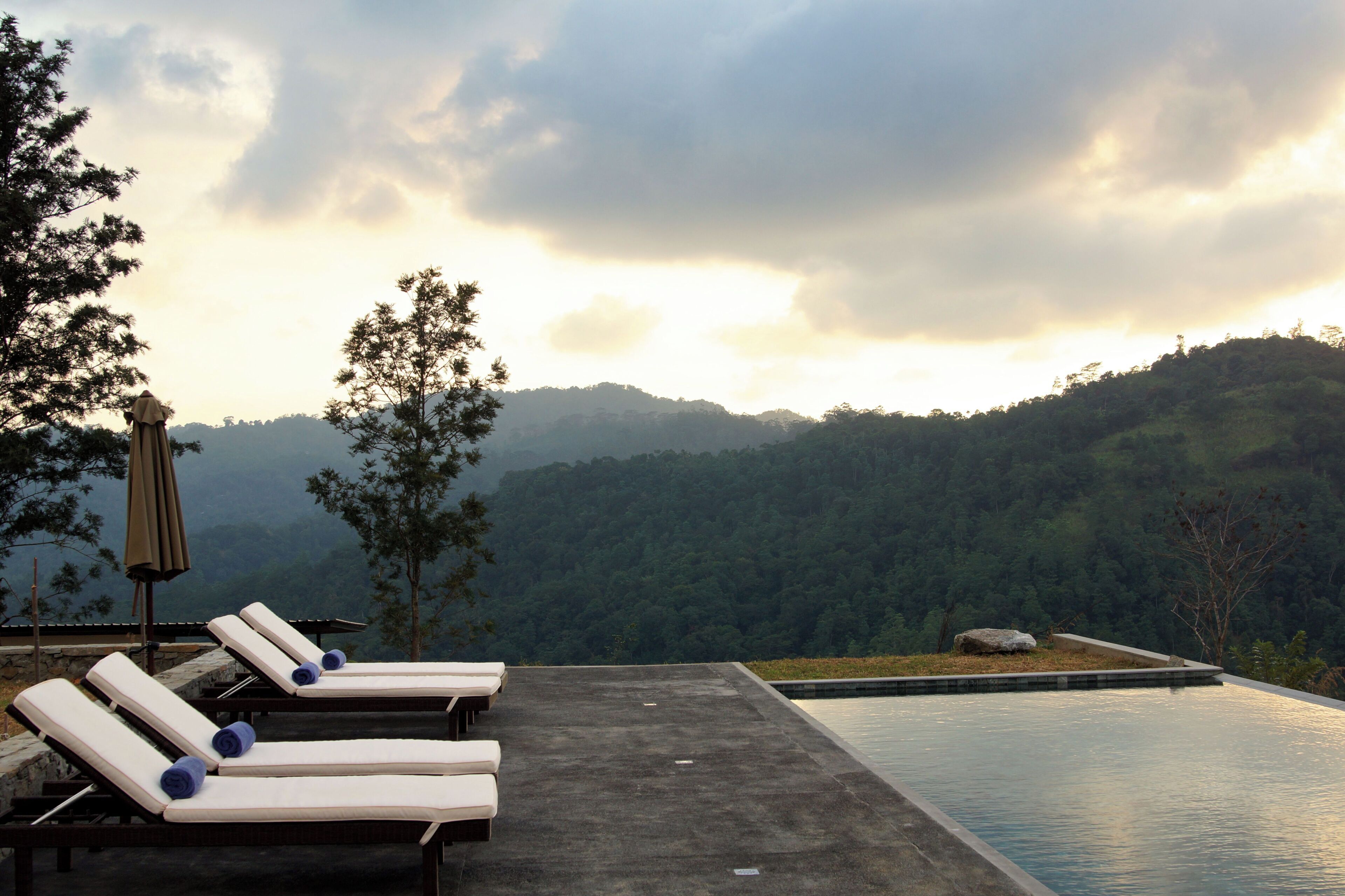 A poolside area with lounge chairs and a view of a forested hillside.