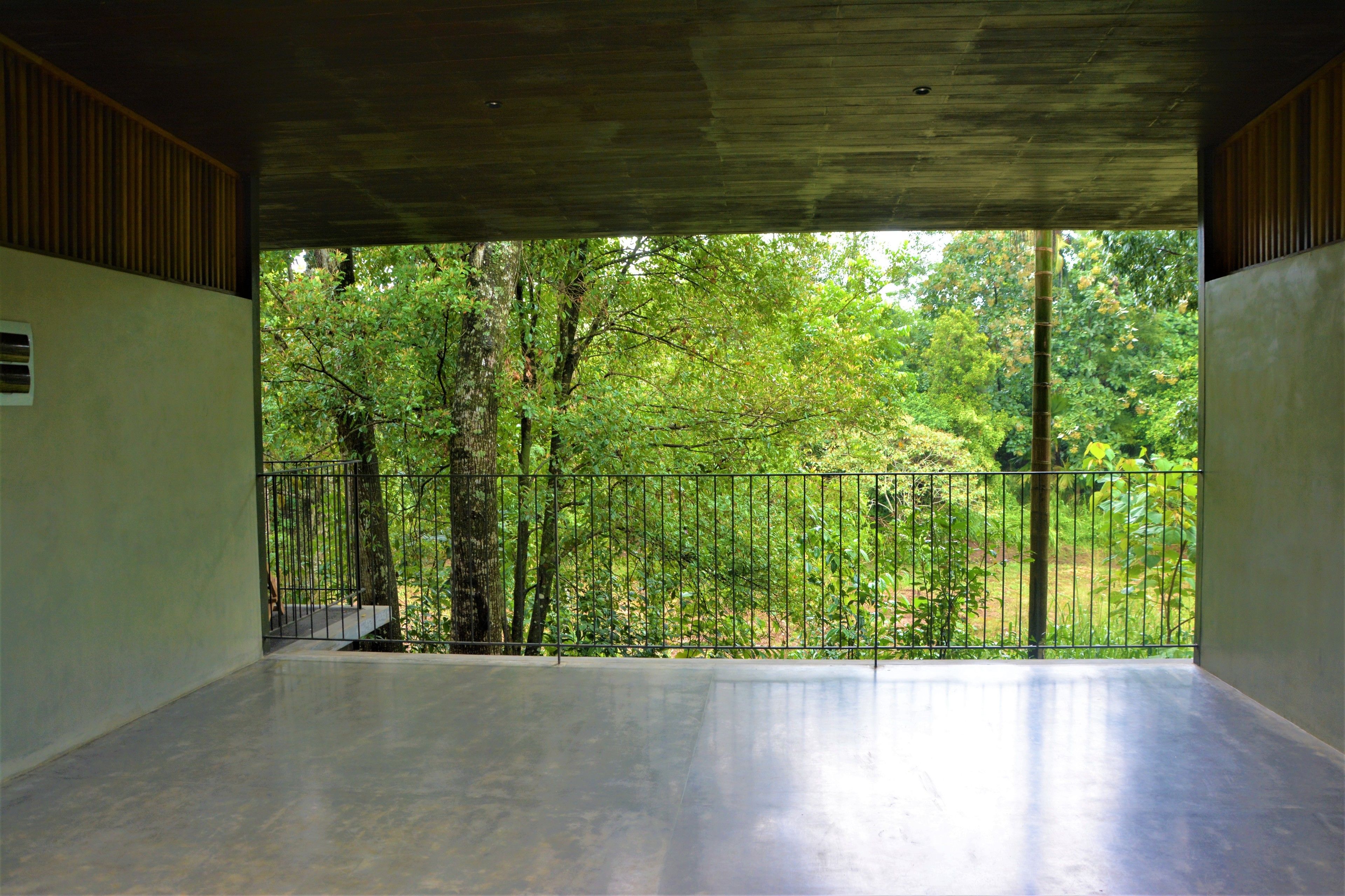 An interior space with a concrete floor and a view of a green forest through a metal fence.