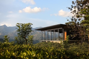 A modern building with large glass windows, surrounded by lush greenery and mountains in the background. - Santani Wellness Kandy (Medadumbara)