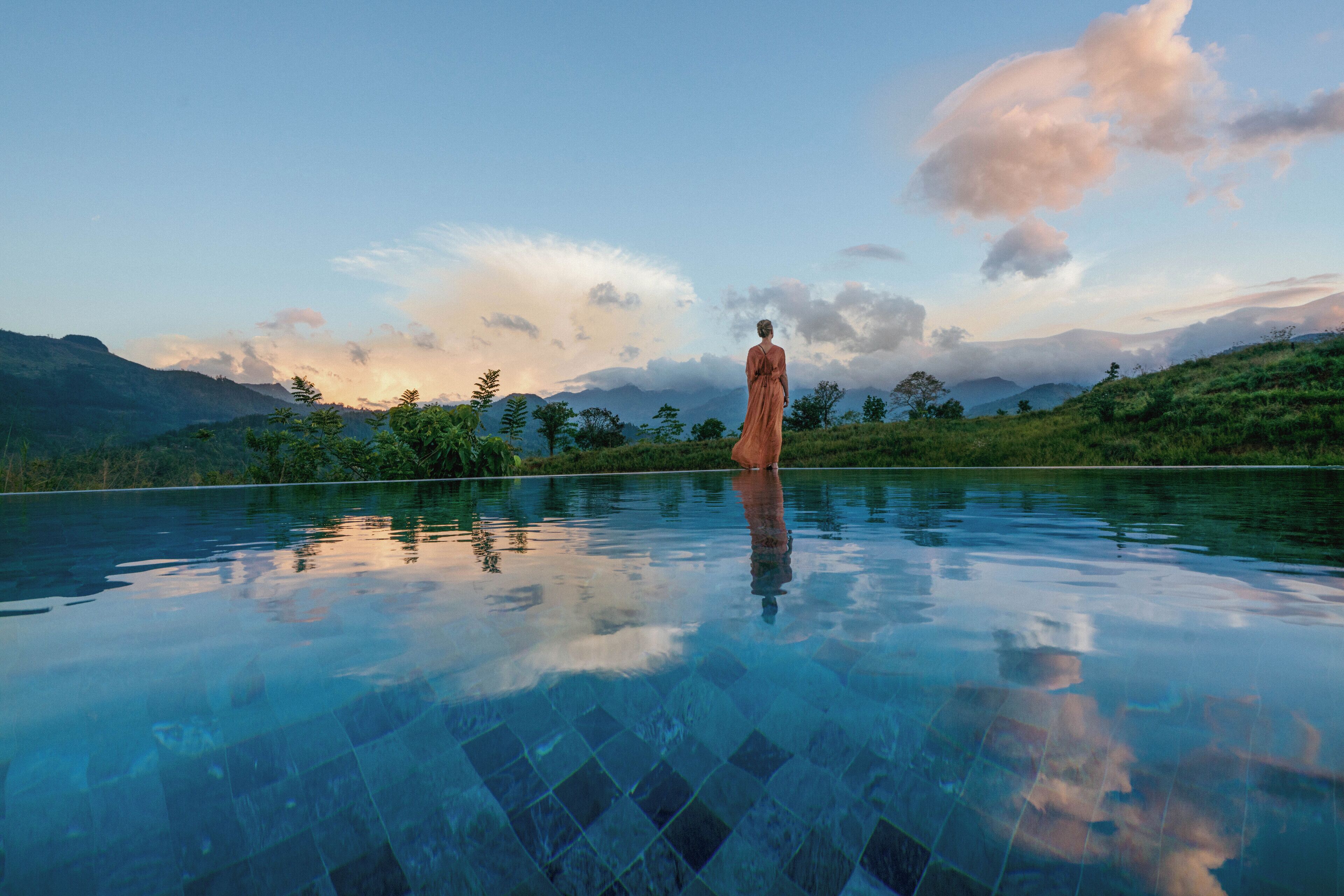 A person standing in a clear pool with a mountainous landscape in the background.