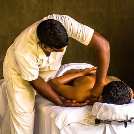 A massage therapy session in a room with a plain wall and a wooden cabinet.
