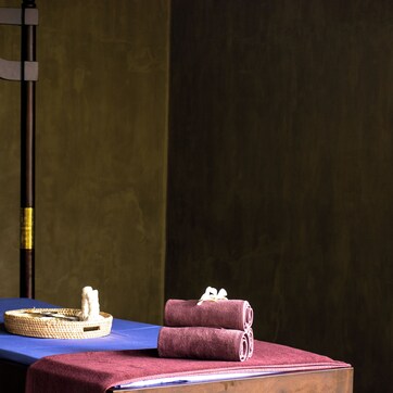 A massage table with a blue sheet, a basket, and rolled towels.
