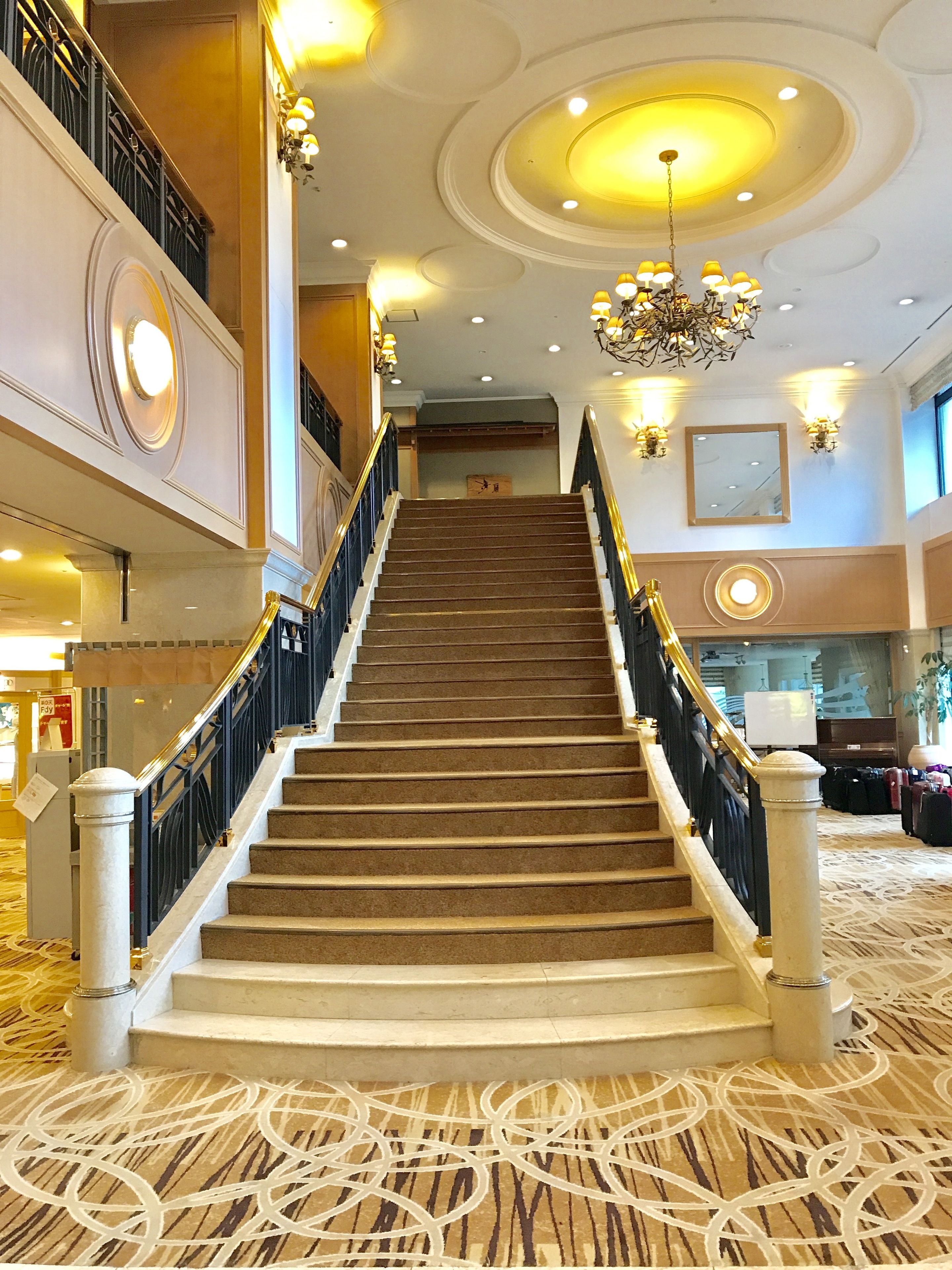 A grand staircase with a carpeted floor, a chandelier, and a mirror on the wall.