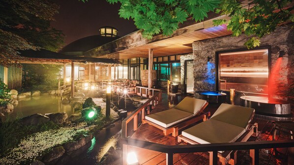 A heated outdoor pool area with lounge chairs, a stone wall, and a wooden deck.