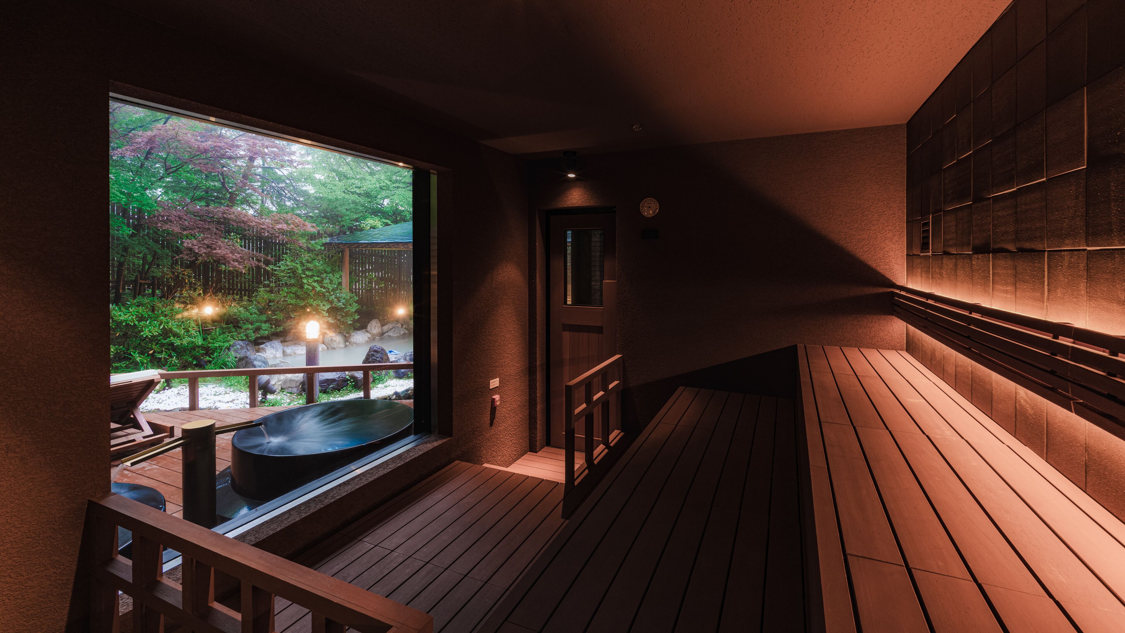 A wooden deck with a hot tub, a view of a garden with trees, and a wooden door.