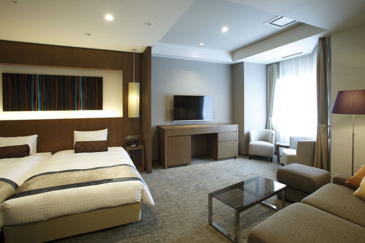 A hotel room with a large bed, a desk, a TV, a sofa, and a coffee table.