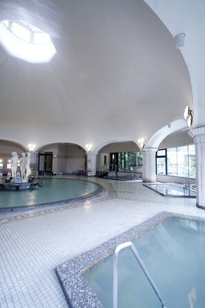 A large indoor swimming pool with multiple lanes, a central statue, and arched ceilings.