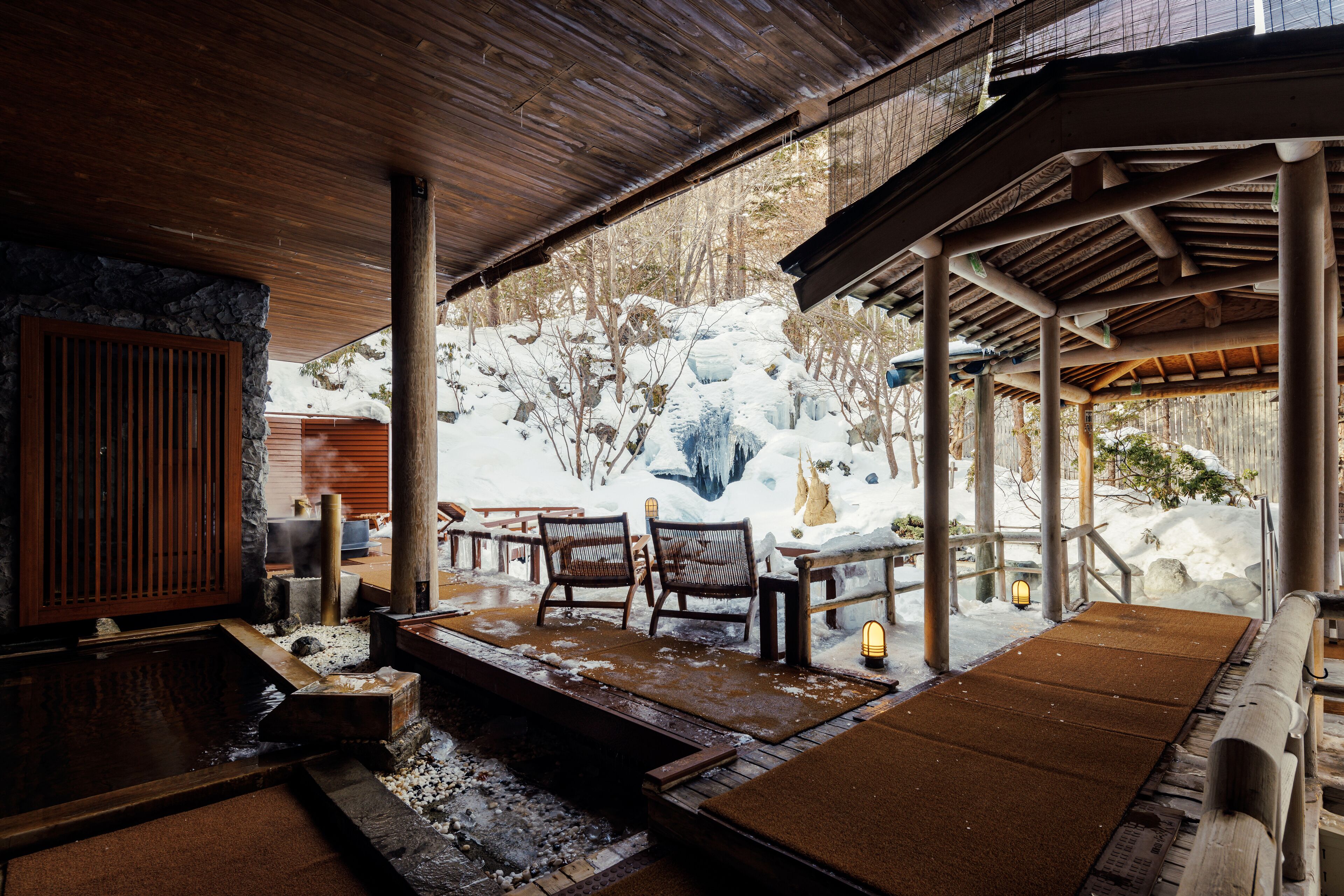 Un’onsen tradizionale giapponese con panche in legno, un muro in pietra e un tetto in legno.