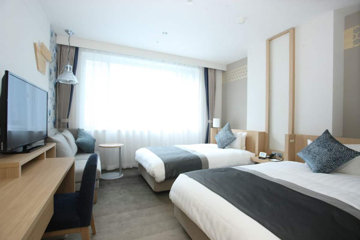 A hotel room with two beds, a desk, a TV, and a small table.