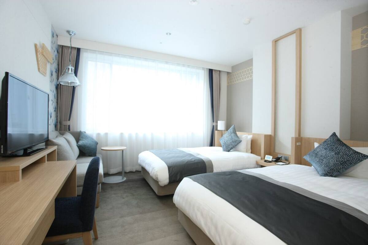 A hotel room with two beds, a desk, a TV, and a small table.