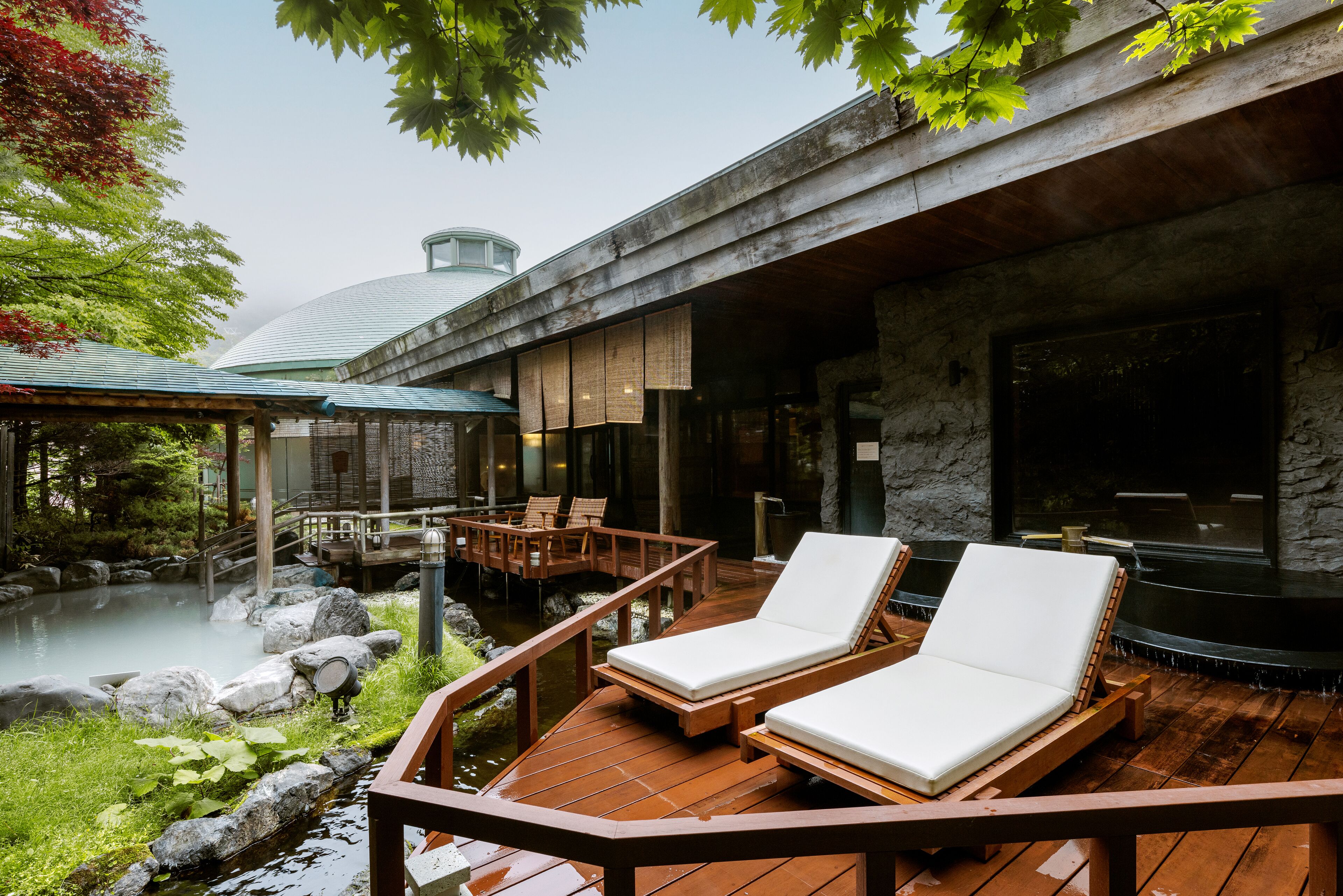 Una terraza de madera con dos sillones, un muro de piedra y un jacuzzi.