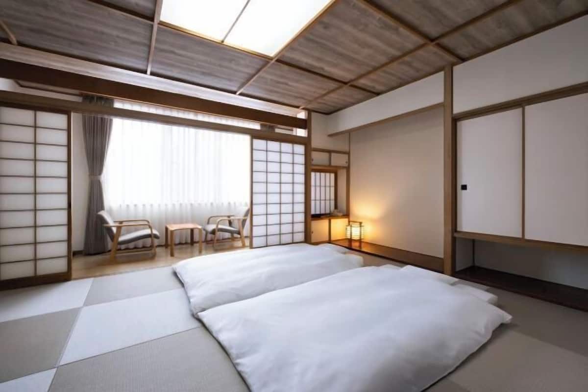 A traditional Japanese-style room with tatami flooring, a low ceiling, sliding doors, and a bed with white bedding.