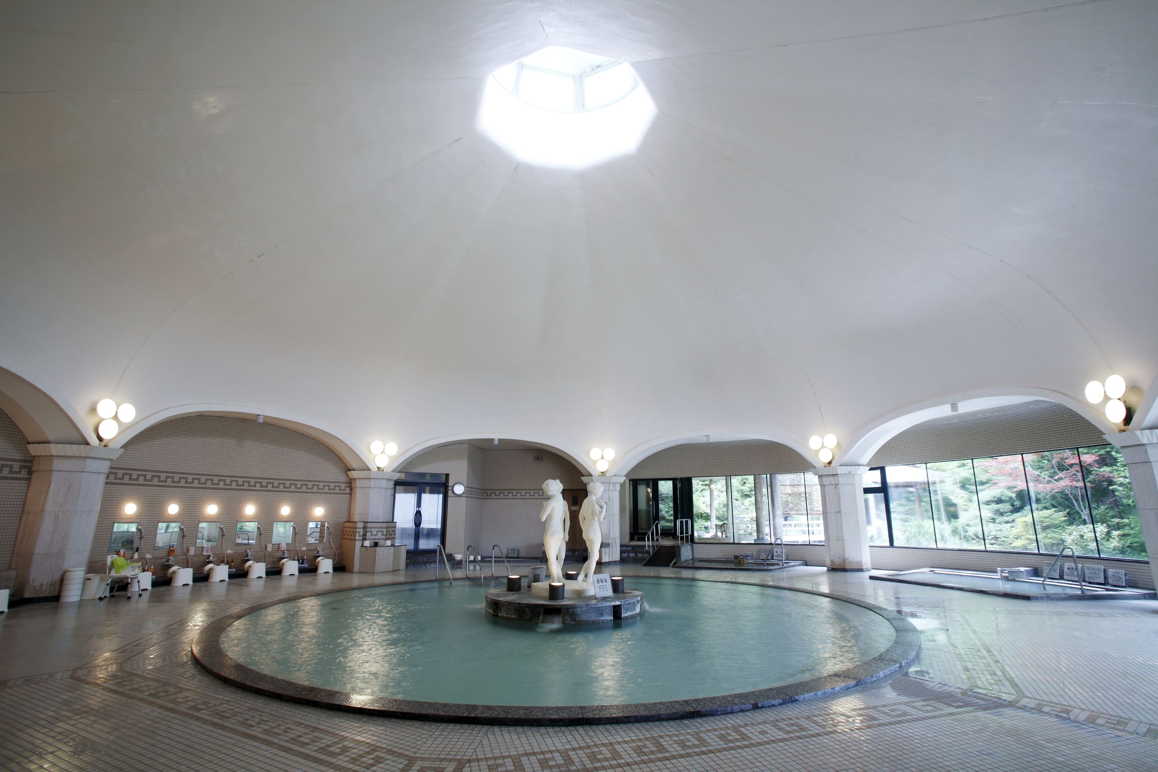 A large indoor swimming pool with a central sculpture, arched ceilings, and multiple seating areas.