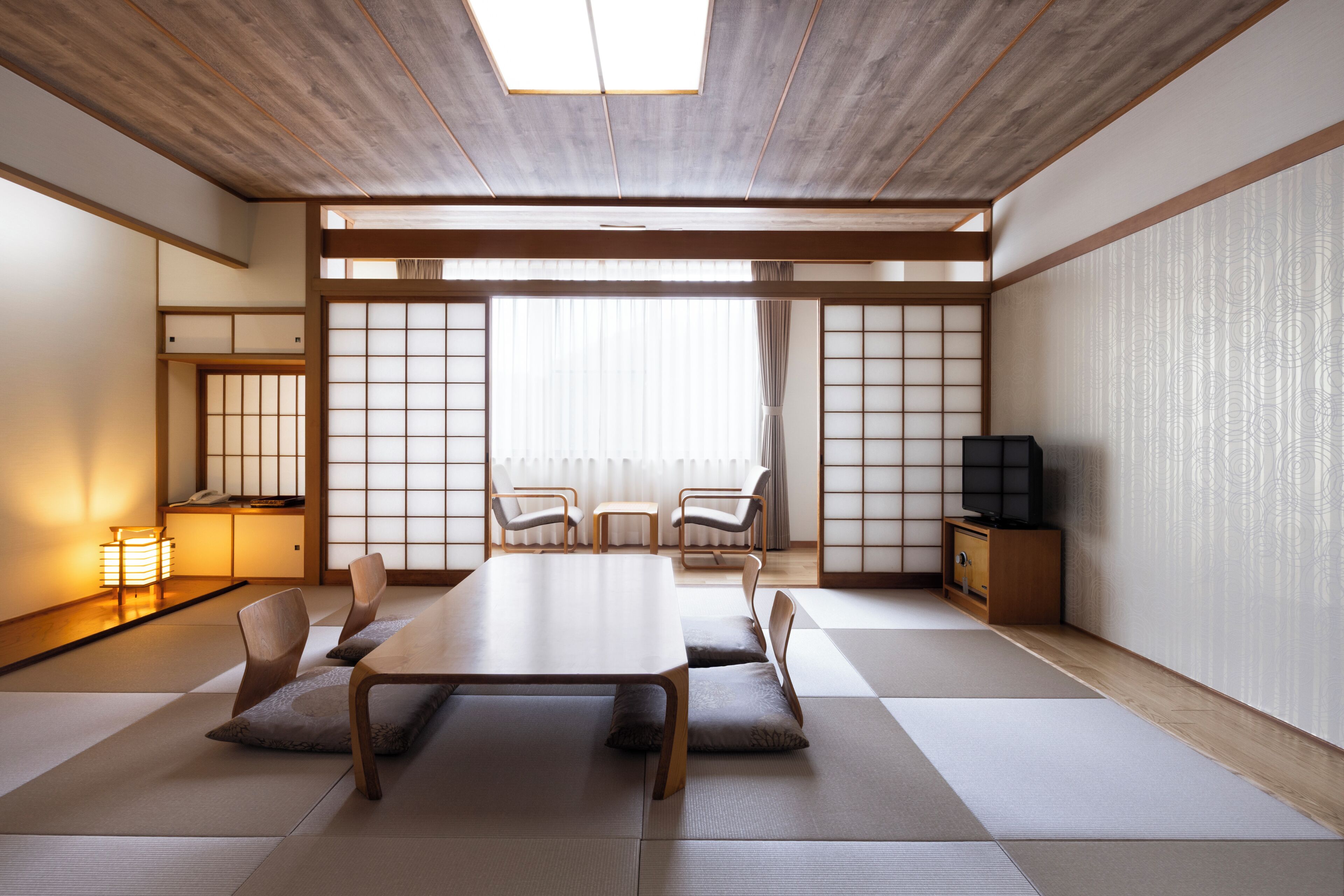 A traditional Japanese room with tatami flooring, a low table, chairs, a television, and sliding doors.