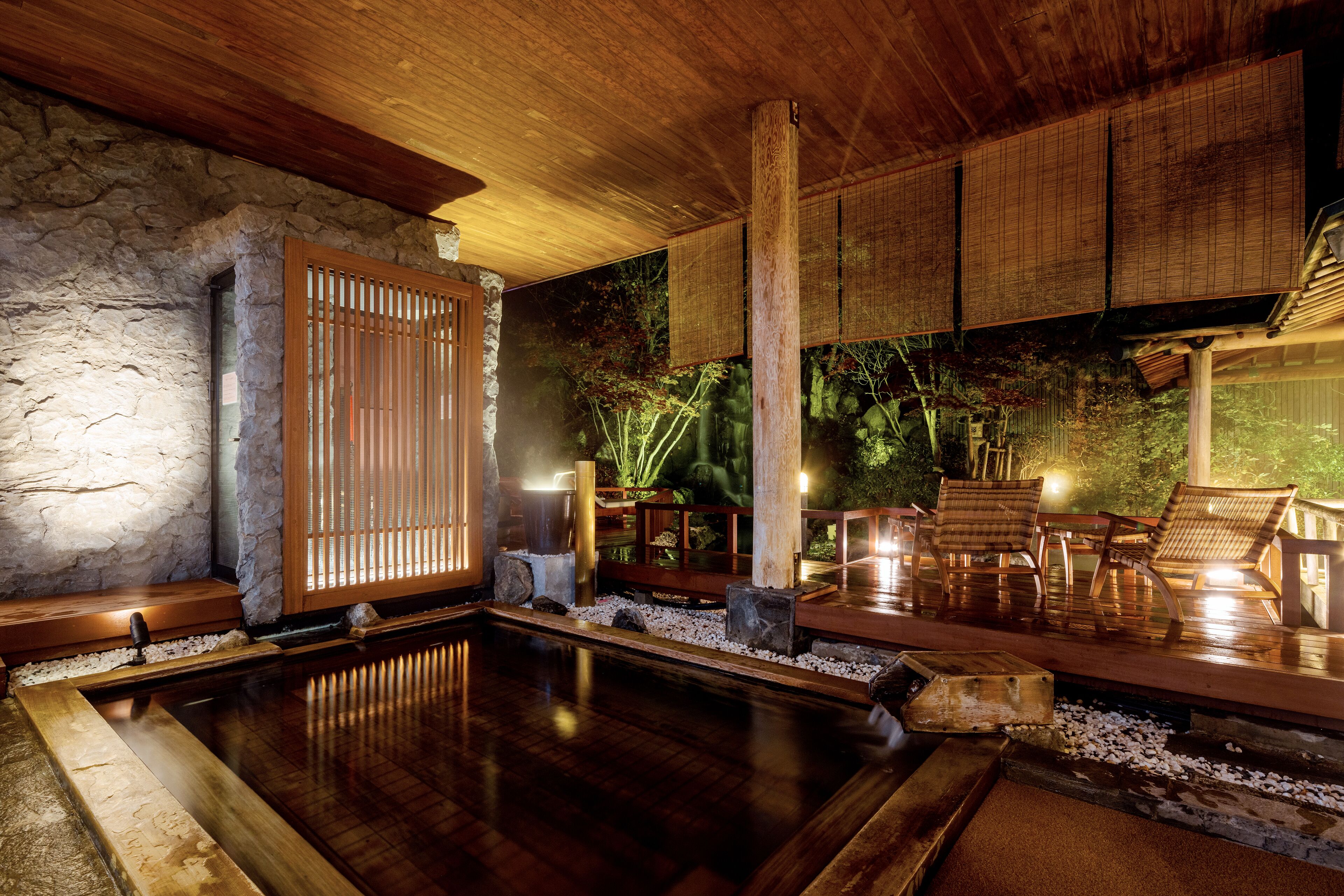 A traditional Japanese onsen with a wooden deck, stone walls, and a view of a garden.