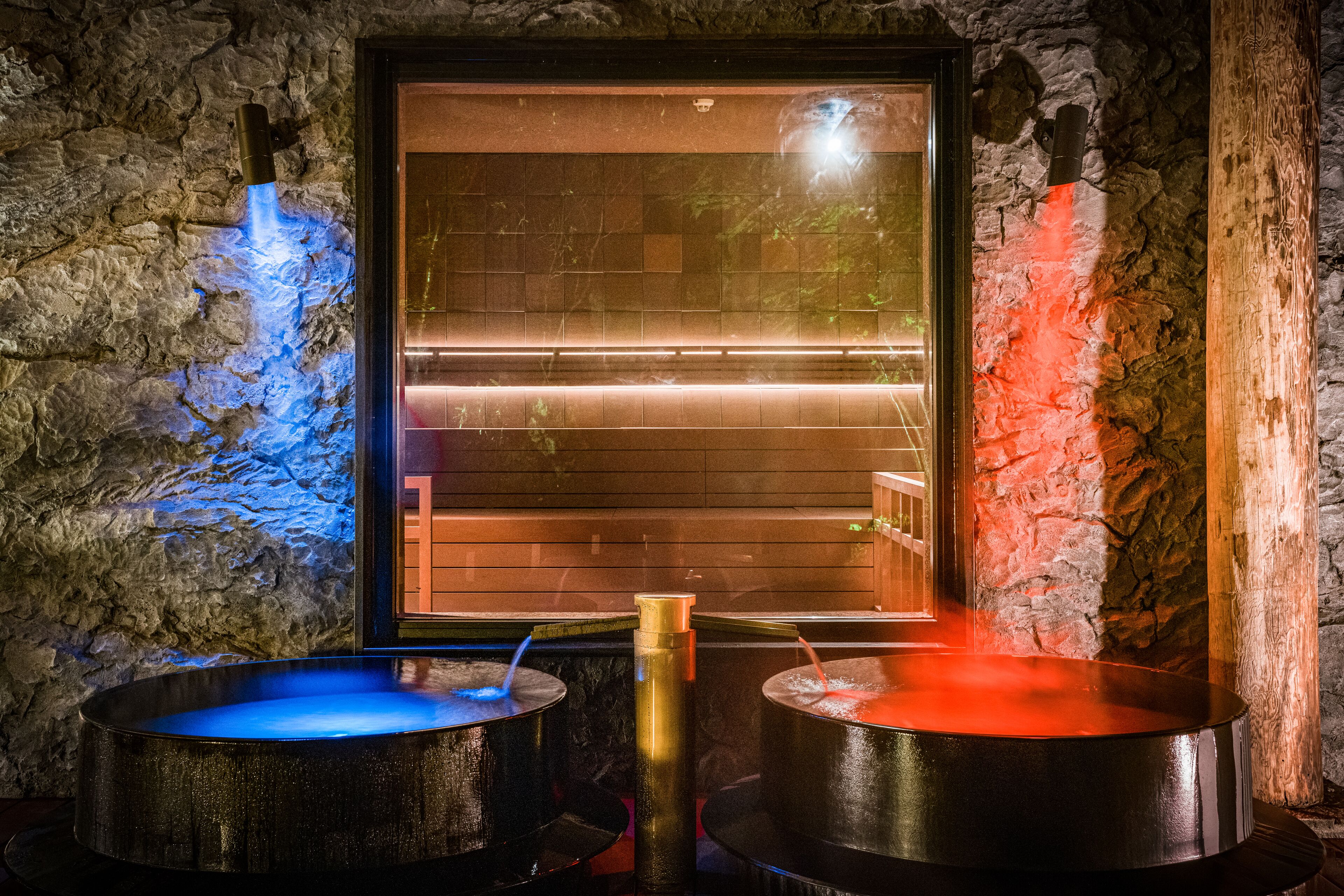 A spa area with two hot tubs, a stone wall, and a wooden door.
