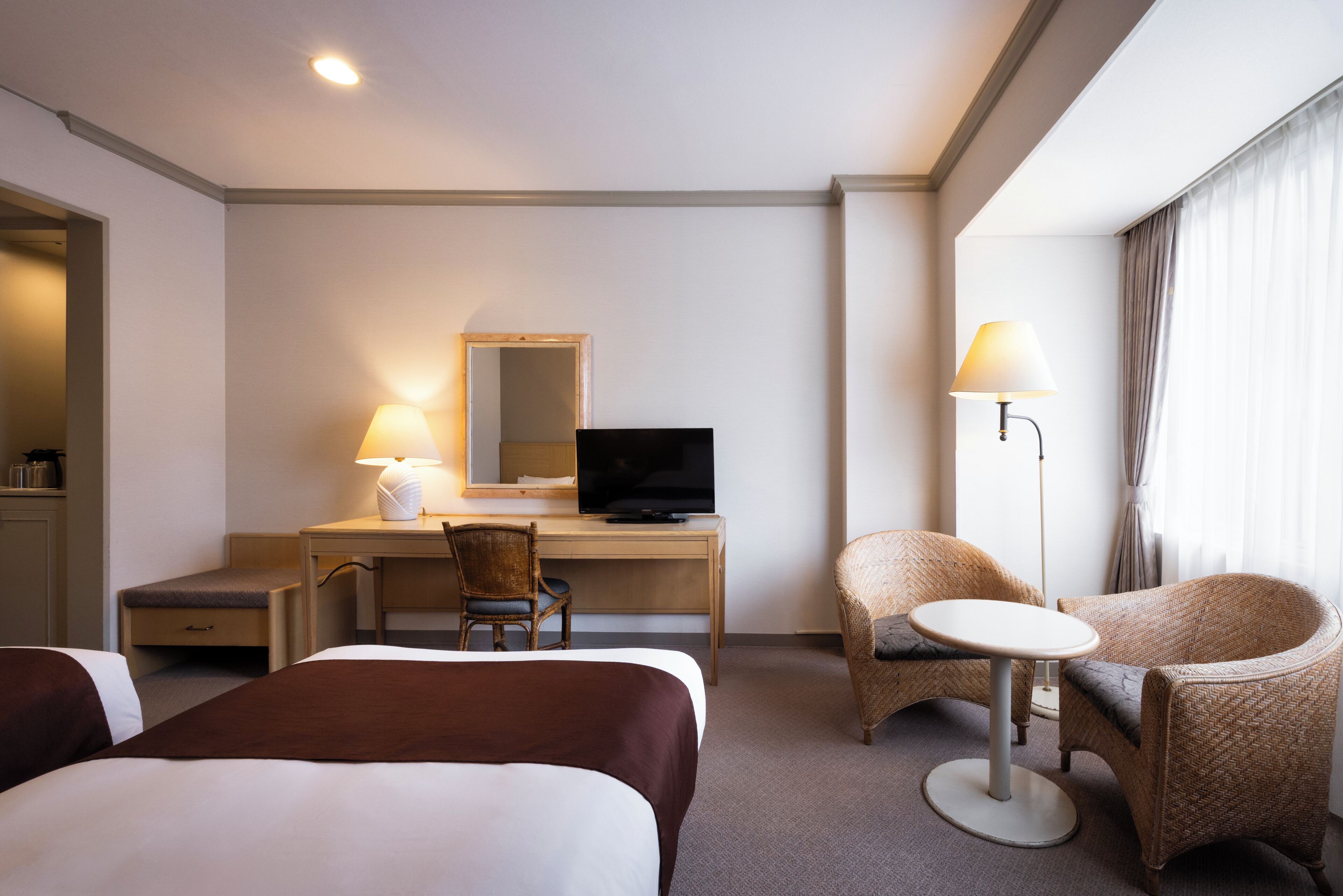 A hotel room with two beds, a desk with a computer, a chair, a small table, and a lamp.
