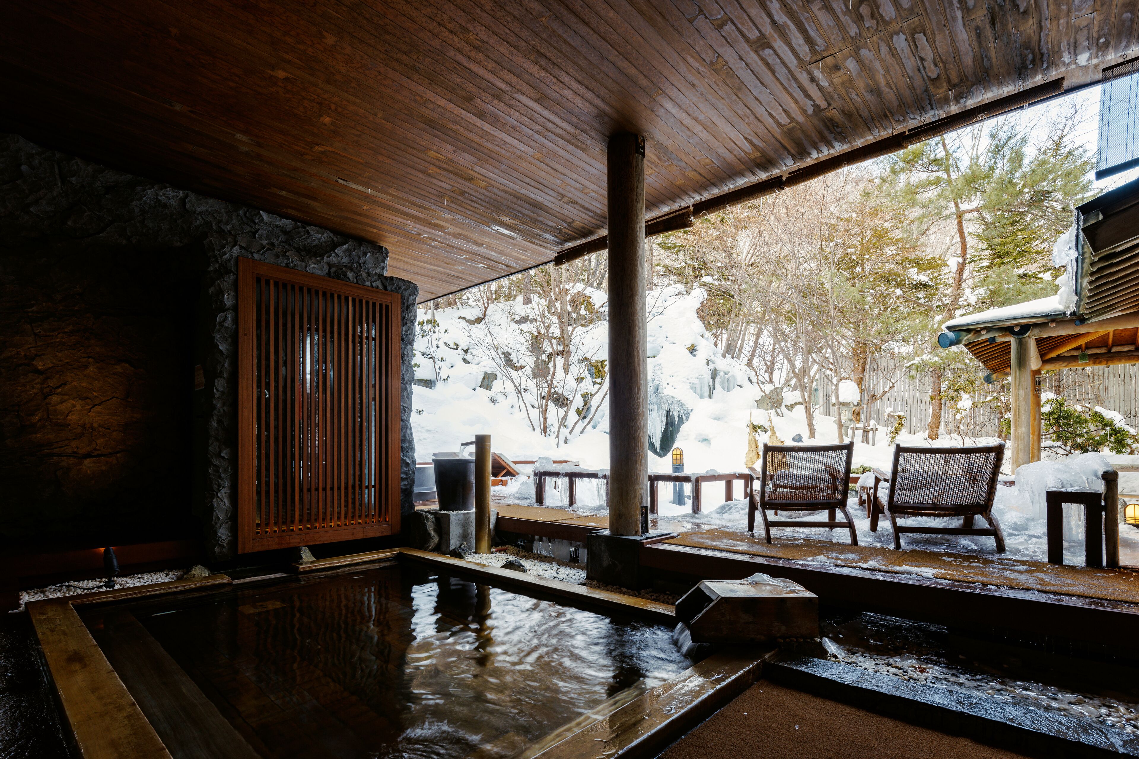 Un interior de madera con una pared de piedra, un banco de madera y una pequeña piscina.