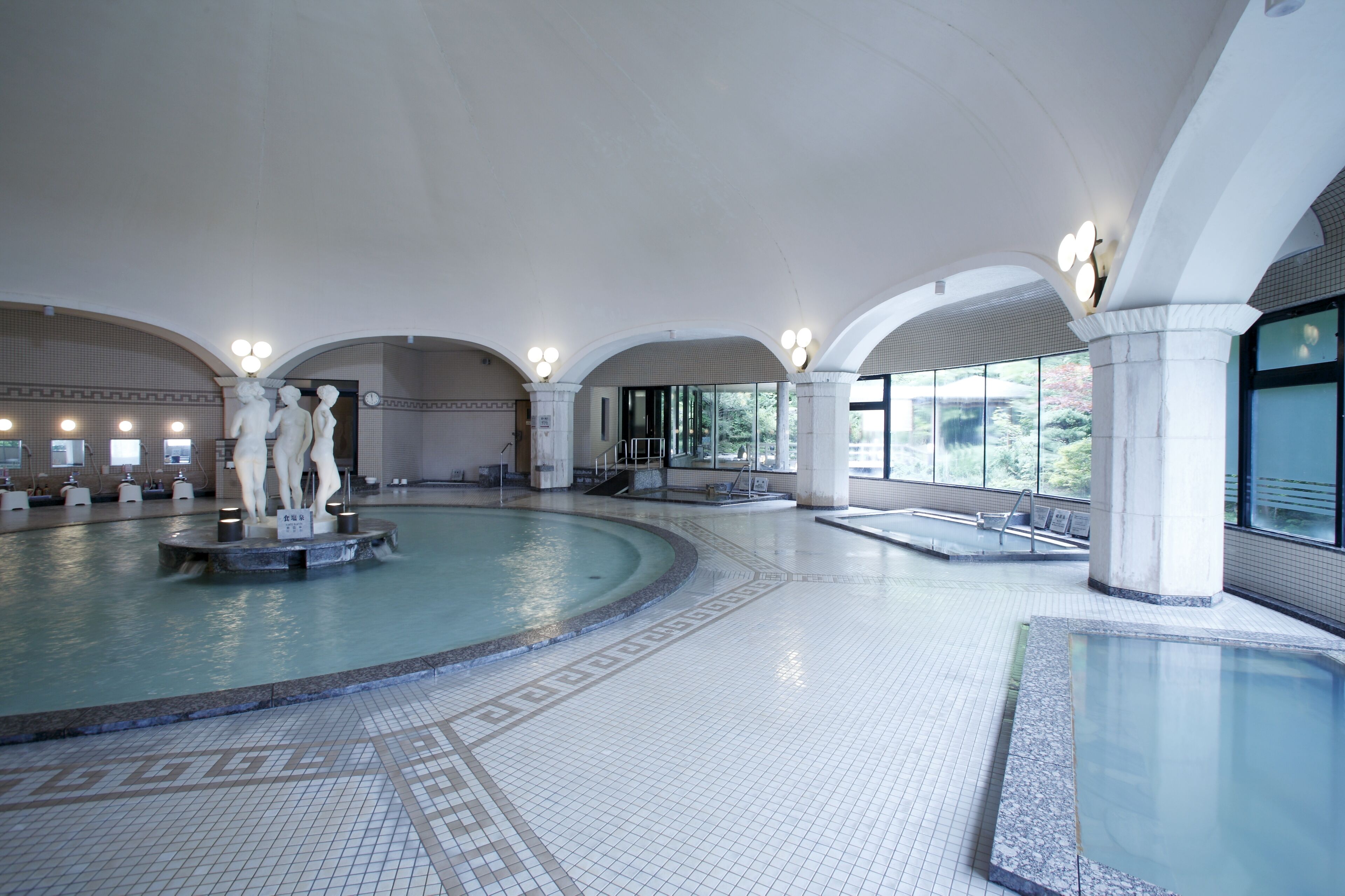 Un'ampia piscina coperta con diverse corsie, una statua al centro e un pavimento piastrellato.