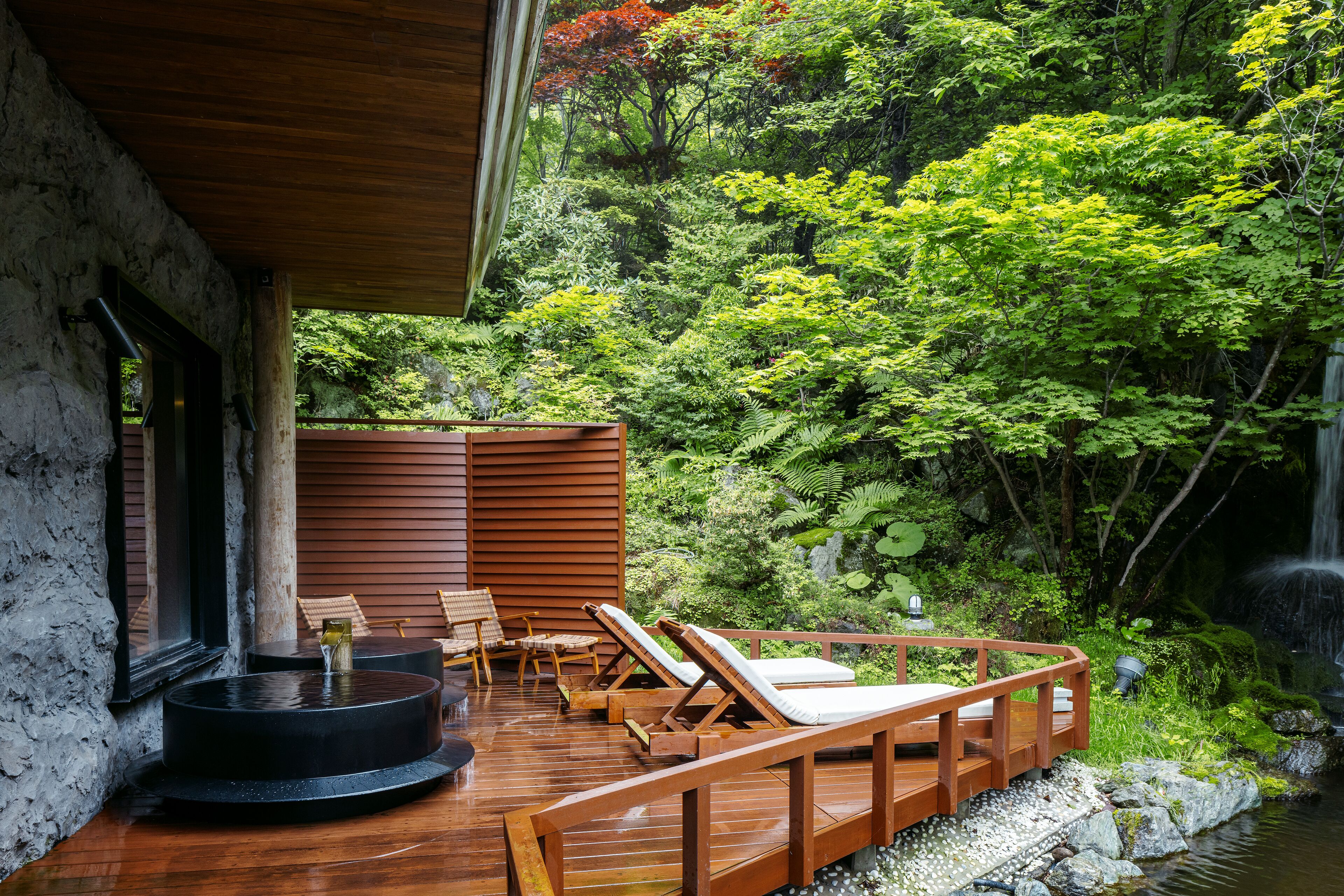 Une terrasse en bois avec des chaises longues donnant sur un jardin luxuriant et une cascade.
