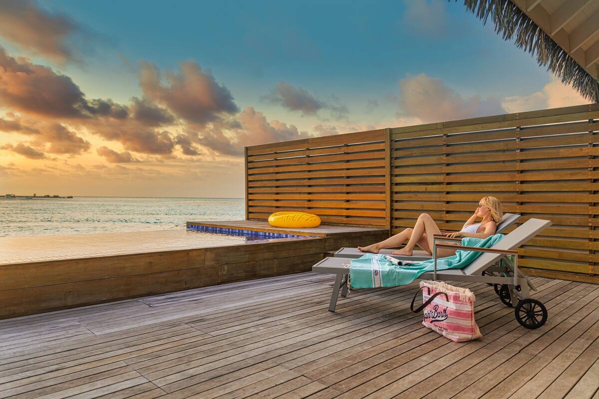 Une terrasse en bois avec une piscine, des chaises longues et une personne se relaxant.