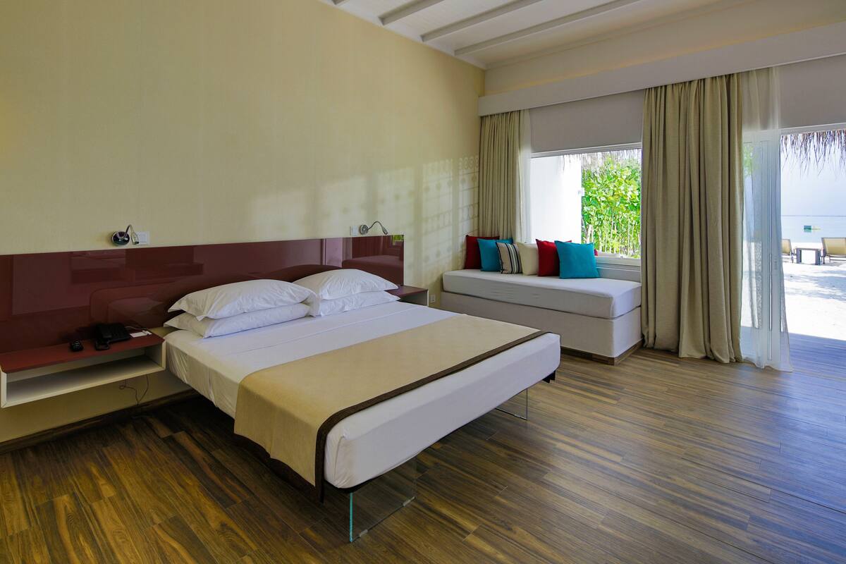 Une chambre d’hôtel avec un grand lit, une table de chevet, un petit canapé et une fenêtre avec des rideaux.