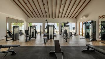 A spacious gym with various exercise equipment, large windows, and a wooden ceiling.