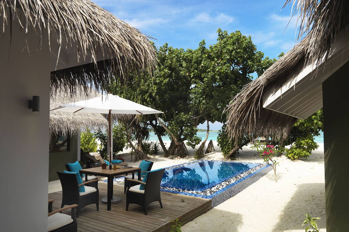 Un espace aménagé au bord de la piscine, avec une terrasse en bois, des chaises longues et une structure dotée d’un toit de chaume.