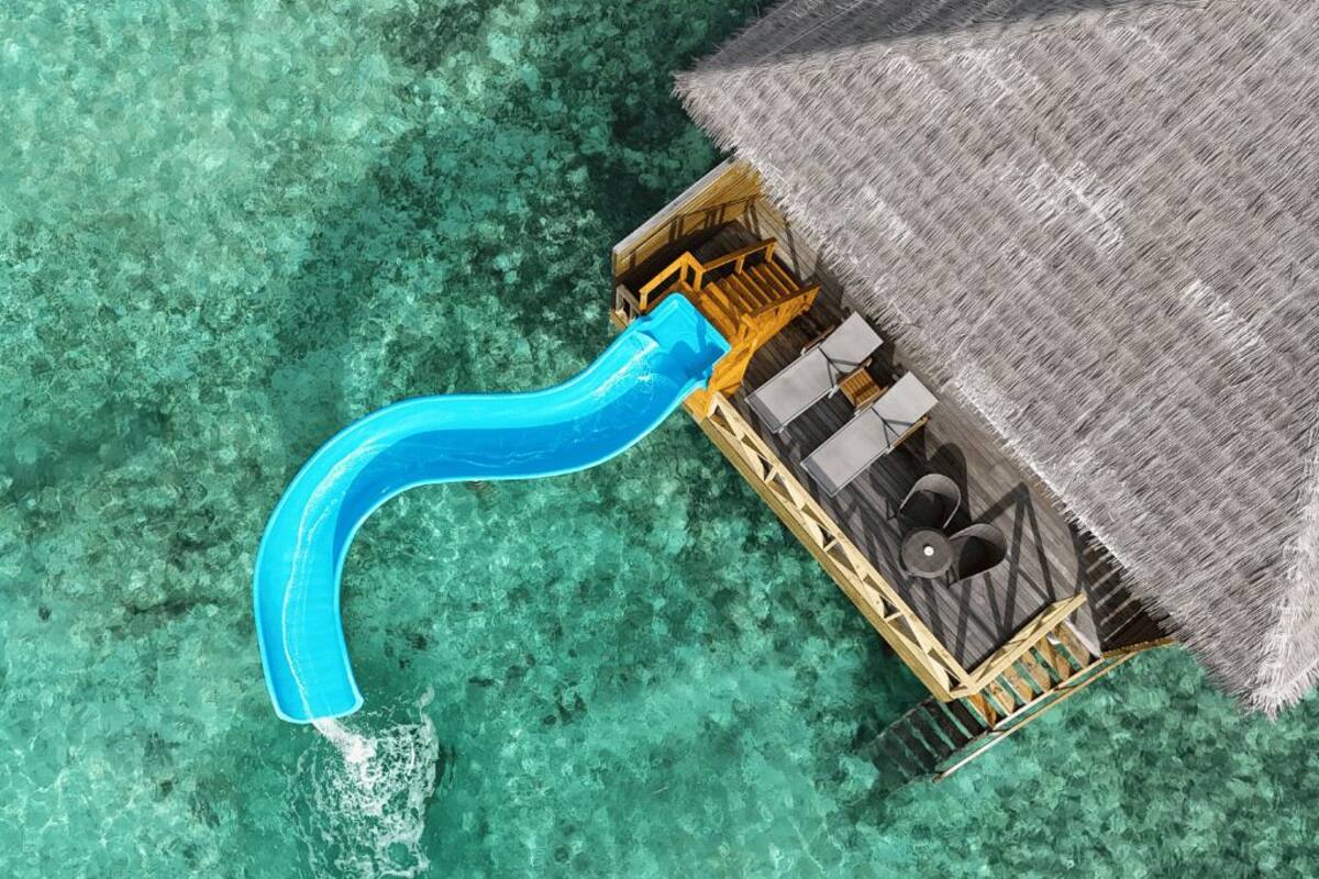 Un bungalow sur pilotis avec un toit de chaume, une piscine avec un toboggan et une terrasse en bois.