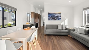 Ein modernes Wohnzimmer mit grauem Sofa, einem Esstisch mit Stühlen und einer Küchenzeile im Hintergrund.