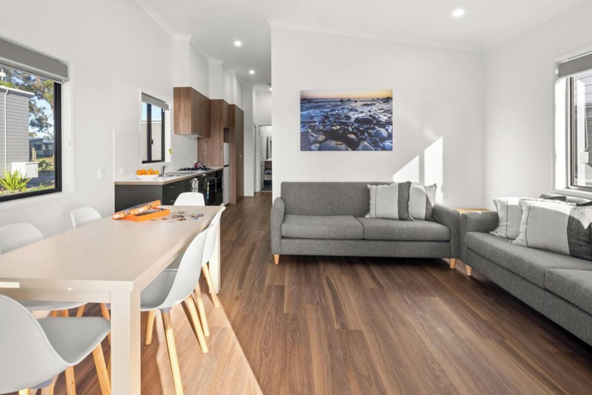 Una sala de estar moderna con un sofá gris, una mesa de comedor con sillas y una zona de cocina al fondo.