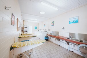 Una cocina limpia y bien iluminada con paredes de azulejos blancos, un lavamanos de acero inoxidable y una lavadora.