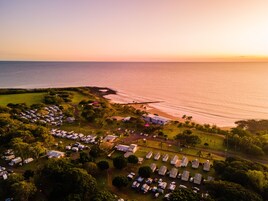 An aerial view of a campground with RVs and mobile homes, a beach, and a pier.