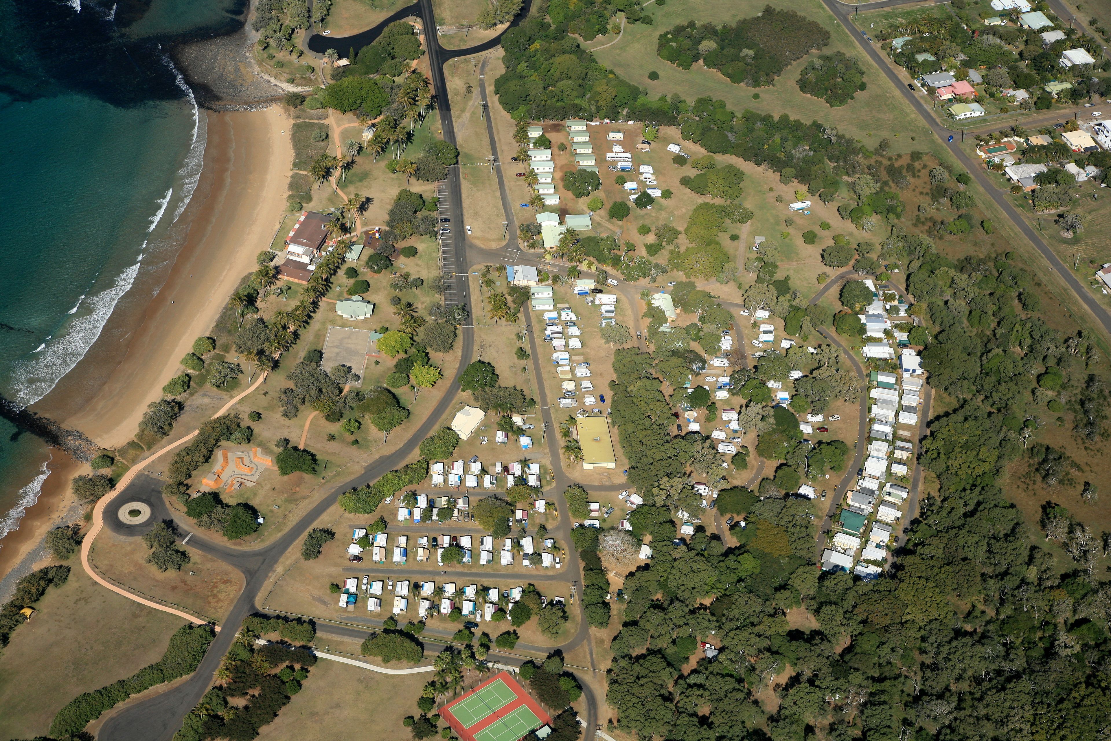 An aerial view of a campground with RVs, a beach, and a tennis court.