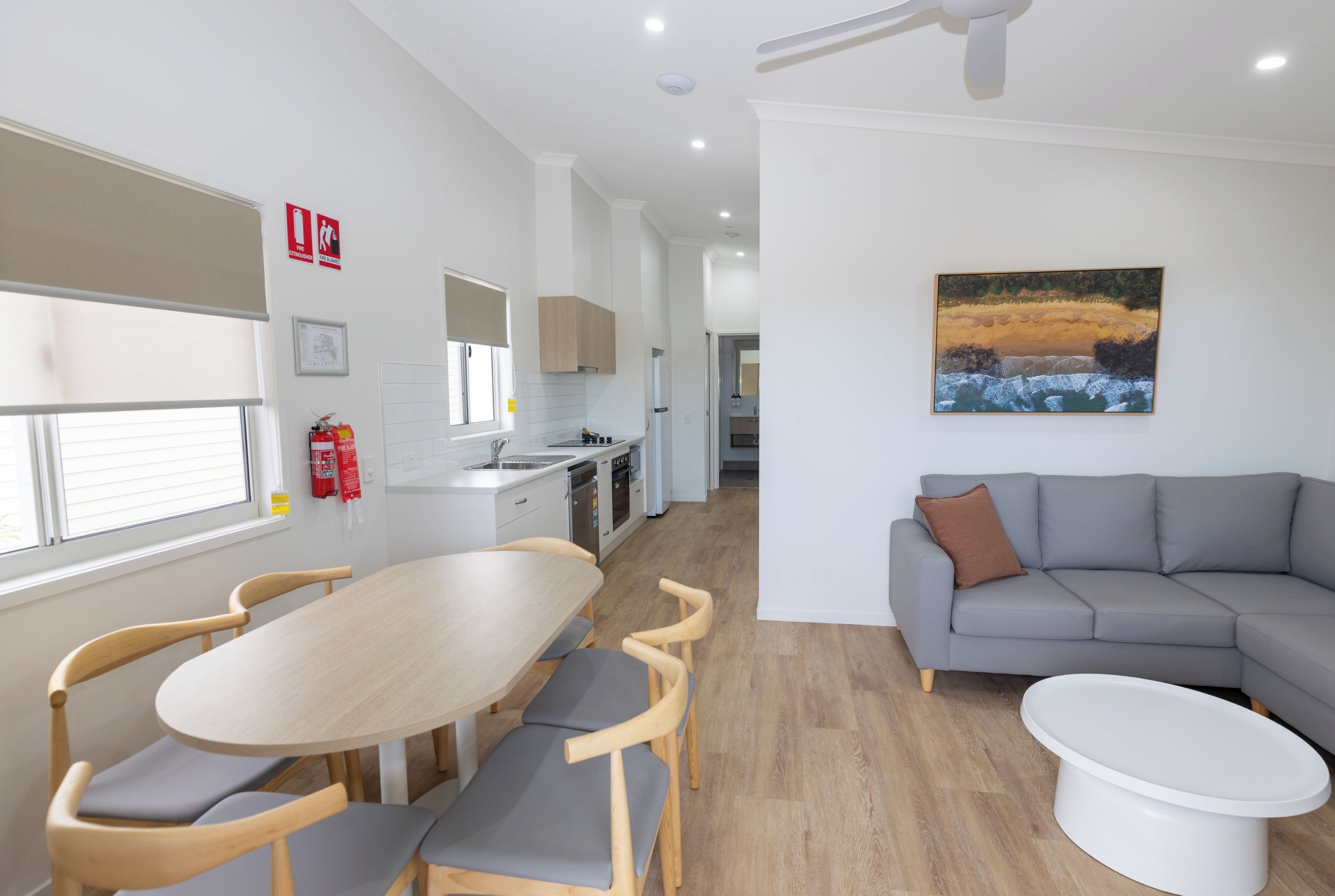 A modern kitchen with a dining area, a gray sofa, and a painting on the wall.